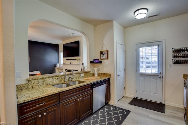 kitchen with light stone countertops, light wood finished floors, arched walkways, a sink, and stainless steel dishwasher