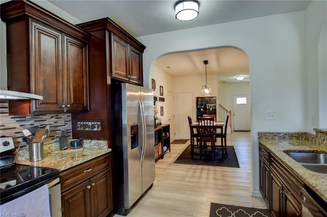 kitchen featuring decorative backsplash, arched walkways, appliances with stainless steel finishes, and light wood-type flooring