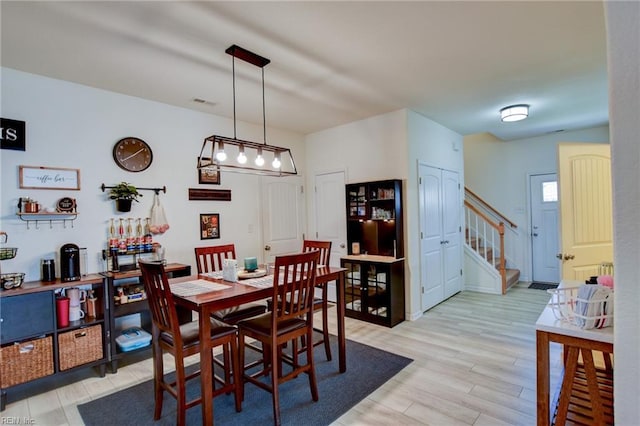 dining area featuring stairway, light wood-style flooring, and visible vents