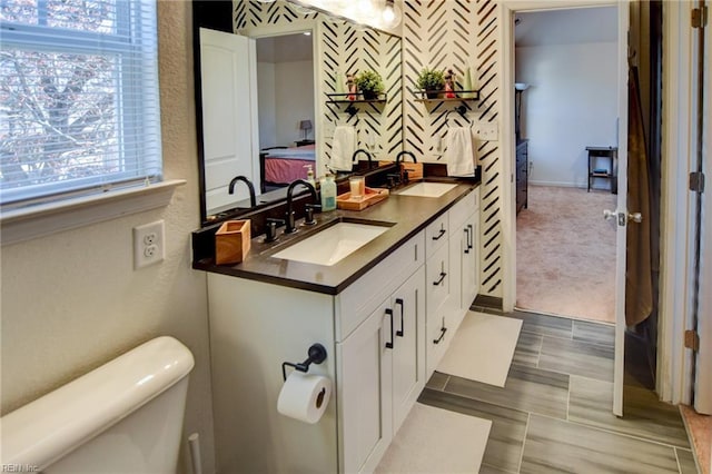 full bathroom featuring toilet, double vanity, connected bathroom, and a sink