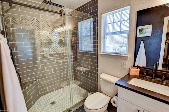 bathroom with vanity, toilet, a textured wall, and a stall shower