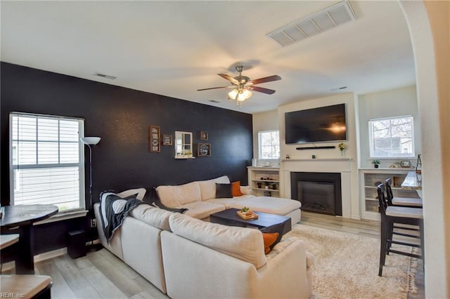 living room featuring a glass covered fireplace, a ceiling fan, visible vents, and a wealth of natural light