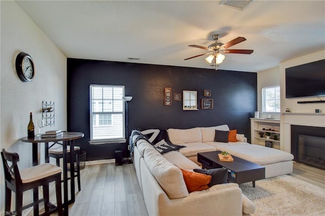 living room featuring visible vents, light wood-style flooring, ceiling fan, and a glass covered fireplace