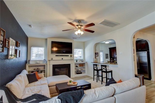 living room featuring visible vents, arched walkways, light wood-style flooring, and a ceiling fan