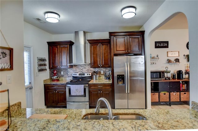 kitchen featuring visible vents, a sink, light stone counters, appliances with stainless steel finishes, and wall chimney range hood