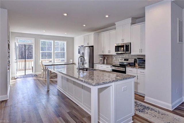 kitchen featuring white cabinetry, an island with sink, backsplash, and stainless steel appliances