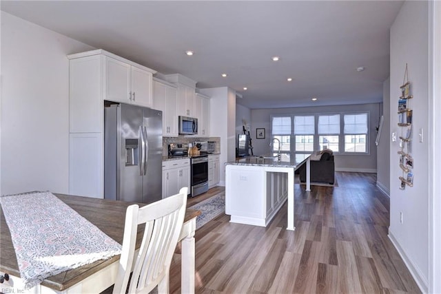 kitchen featuring a sink, stainless steel appliances, white cabinets, light wood finished floors, and decorative backsplash