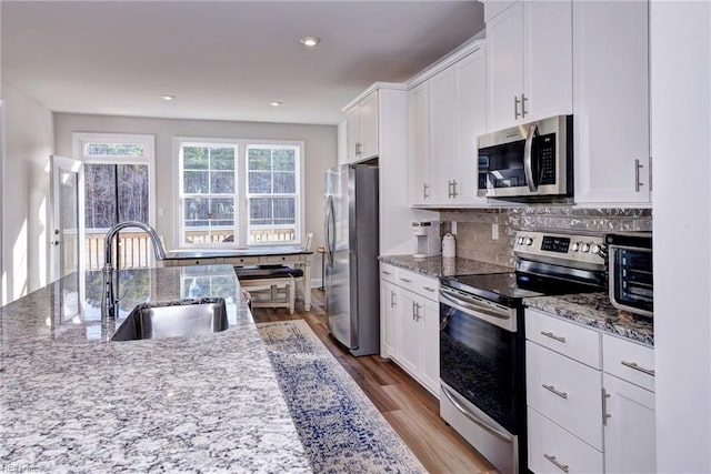 kitchen featuring light wood finished floors, a sink, stainless steel appliances, white cabinetry, and tasteful backsplash