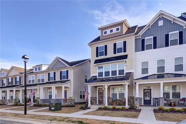 townhome / multi-family property featuring a standing seam roof, a residential view, covered porch, stone siding, and board and batten siding