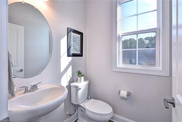 half bath featuring toilet, baseboards, and a sink