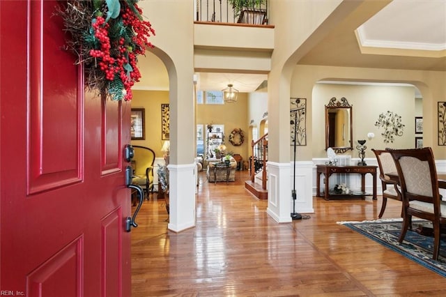 entrance foyer featuring arched walkways, wainscoting, crown molding, and wood finished floors