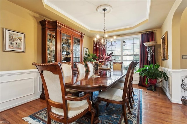 dining space featuring a wainscoted wall, an inviting chandelier, a tray ceiling, and wood finished floors