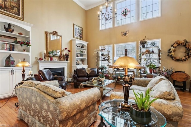 living room featuring a notable chandelier, a warm lit fireplace, wood finished floors, a high ceiling, and crown molding