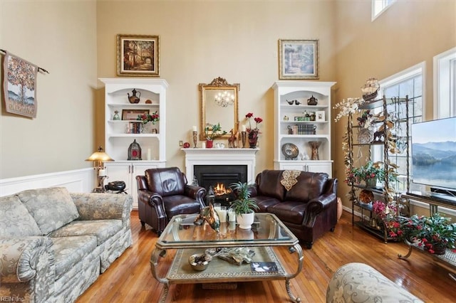 living room featuring a wainscoted wall, a warm lit fireplace, and wood finished floors