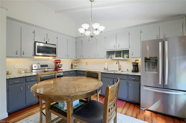 kitchen with light wood-type flooring, a notable chandelier, a sink, appliances with stainless steel finishes, and decorative backsplash