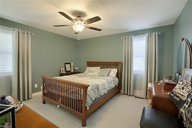 carpeted bedroom featuring visible vents, a textured ceiling, baseboards, and a ceiling fan