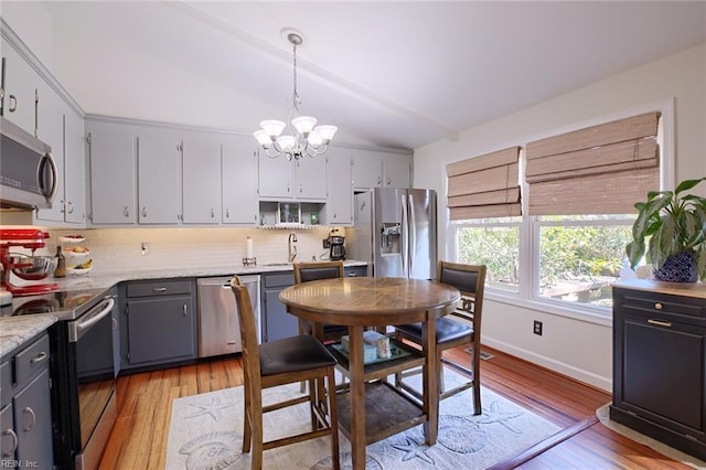 kitchen featuring backsplash, lofted ceiling, gray cabinets, an inviting chandelier, and stainless steel appliances