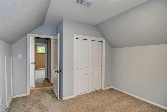 additional living space with visible vents, a textured ceiling, baseboards, light colored carpet, and vaulted ceiling