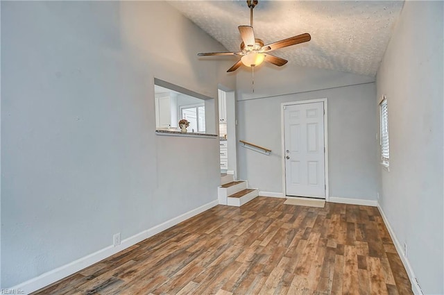 spare room with a ceiling fan, wood finished floors, baseboards, stairs, and vaulted ceiling