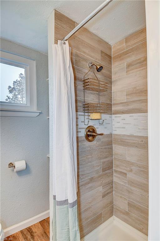 full bathroom featuring a textured ceiling, wood finished floors, baseboards, and tiled shower