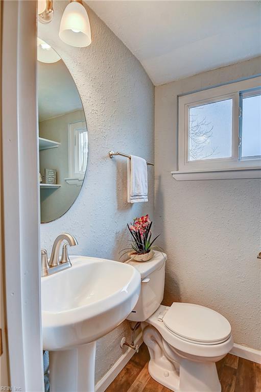 half bathroom with a sink, toilet, wood finished floors, and a textured wall