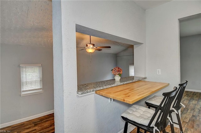 dining room featuring baseboards, a textured ceiling, dark wood finished floors, and a ceiling fan