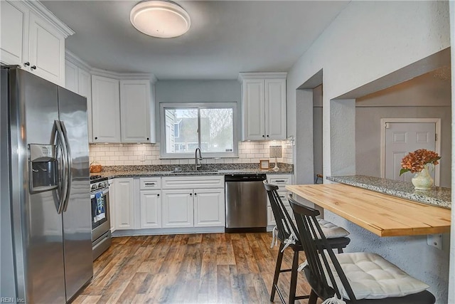 kitchen with dark wood-style flooring, a sink, stainless steel appliances, white cabinetry, and tasteful backsplash