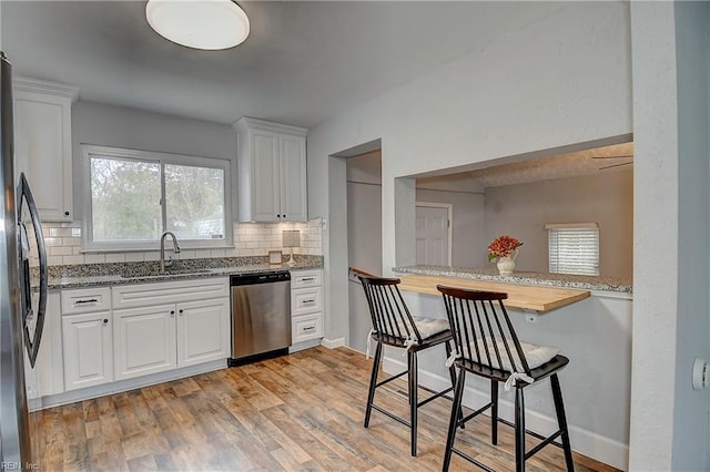 kitchen featuring light wood-type flooring, a sink, backsplash, stainless steel appliances, and white cabinets