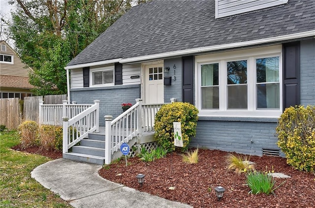 view of exterior entry featuring brick siding, crawl space, a shingled roof, and fence