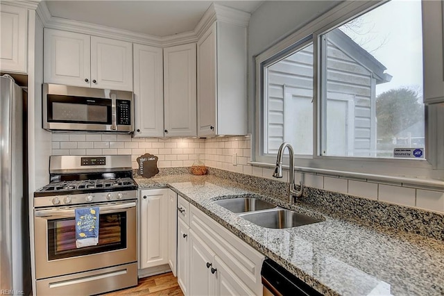 kitchen with light stone counters, a sink, decorative backsplash, appliances with stainless steel finishes, and white cabinetry