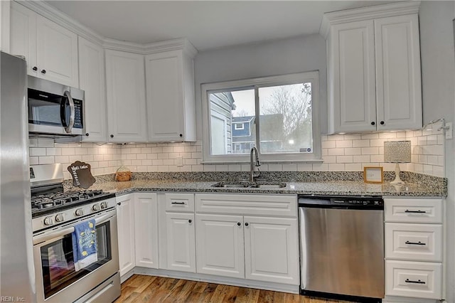 kitchen with light stone counters, appliances with stainless steel finishes, white cabinetry, and a sink