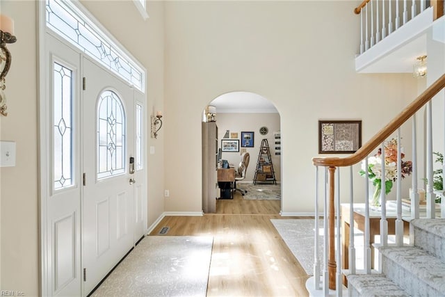 foyer entrance with stairs, light wood-style floors, baseboards, arched walkways, and a towering ceiling