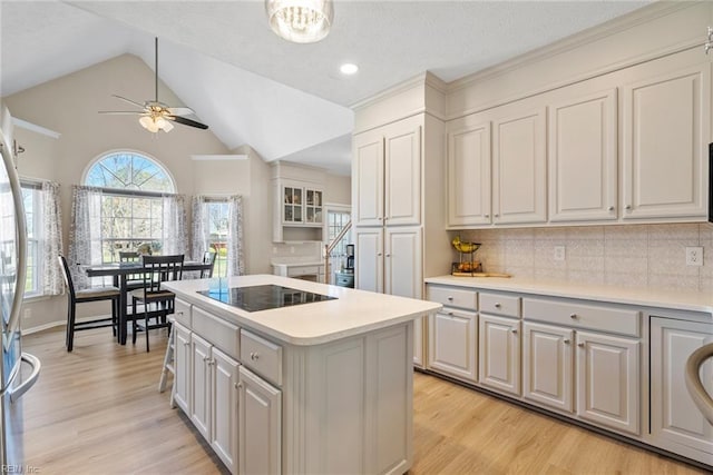 kitchen featuring vaulted ceiling, black electric stovetop, a center island, light wood-style flooring, and ceiling fan