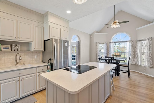 kitchen featuring black electric cooktop, light countertops, light wood-type flooring, a sink, and freestanding refrigerator