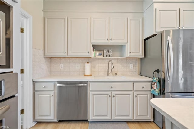 kitchen featuring light countertops, a sink, light wood finished floors, stainless steel appliances, and decorative backsplash