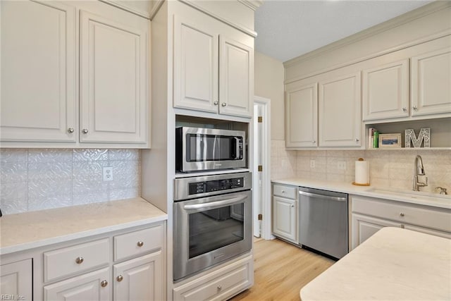 kitchen with light countertops, a sink, stainless steel appliances, light wood-style floors, and decorative backsplash