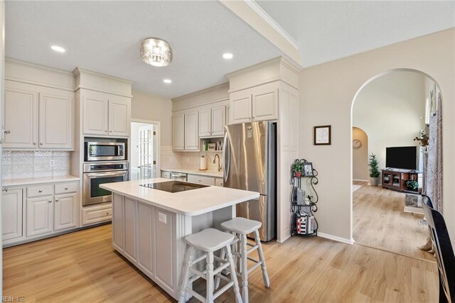 kitchen with light countertops, light wood-style flooring, stainless steel appliances, a kitchen island, and arched walkways