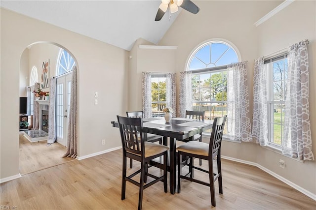 dining room featuring arched walkways, a wealth of natural light, light wood-style floors, and a ceiling fan
