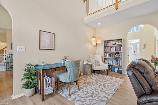 office featuring baseboards, wood finished floors, arched walkways, and a towering ceiling