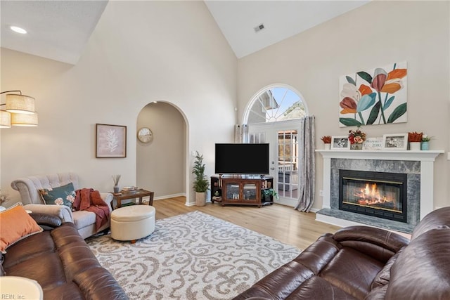 living area with high vaulted ceiling, visible vents, a premium fireplace, wood finished floors, and arched walkways