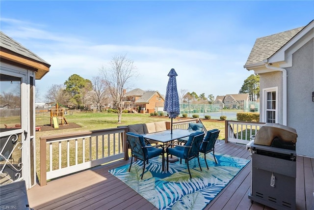 wooden deck with a playground, area for grilling, outdoor dining space, and a lawn