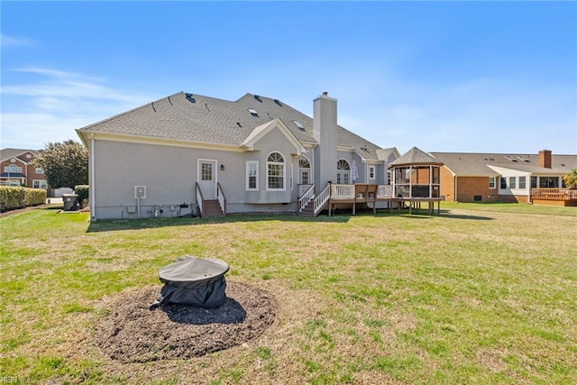 rear view of property with a wooden deck, entry steps, a chimney, stucco siding, and a yard