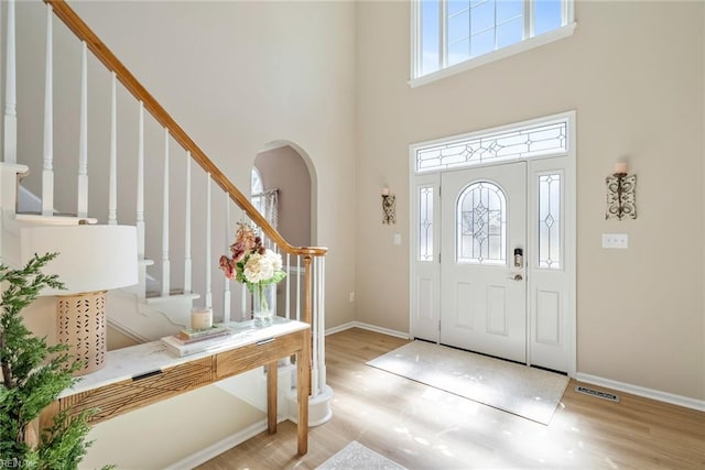 foyer entrance featuring arched walkways, baseboards, wood finished floors, and stairway