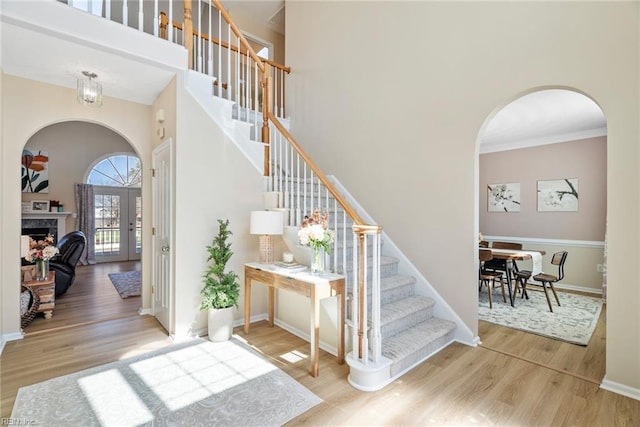 stairs featuring a fireplace, wood finished floors, arched walkways, and a towering ceiling