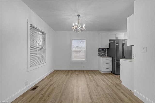 unfurnished dining area with light wood-type flooring, visible vents, baseboards, and a notable chandelier