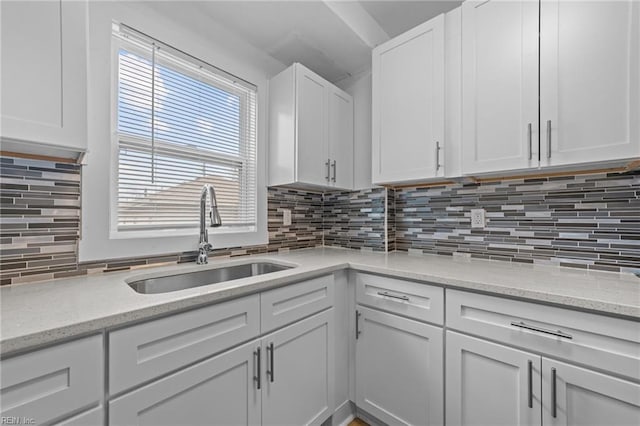 kitchen featuring a sink, light stone counters, tasteful backsplash, and white cabinets