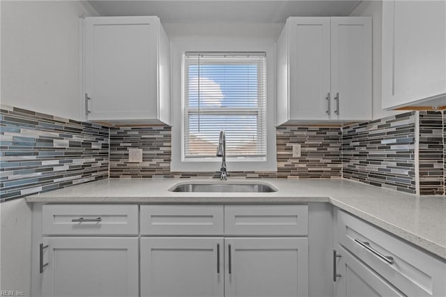 kitchen featuring white cabinetry, light stone countertops, tasteful backsplash, and a sink