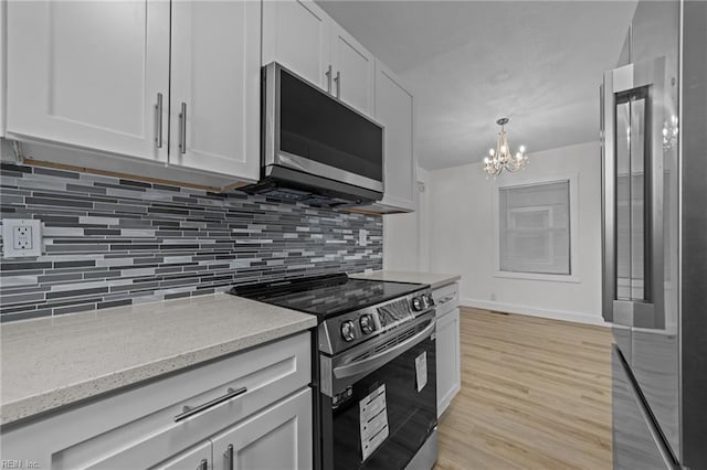 kitchen featuring light wood-style floors, appliances with stainless steel finishes, decorative backsplash, light stone countertops, and a chandelier