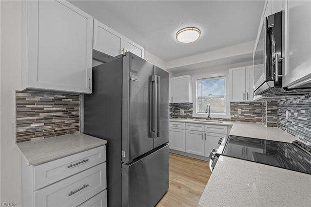 kitchen featuring a sink, appliances with stainless steel finishes, white cabinetry, tasteful backsplash, and light wood-type flooring