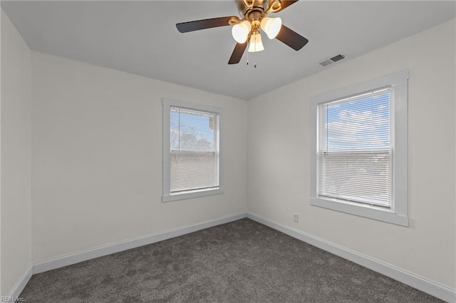 empty room with dark colored carpet, visible vents, plenty of natural light, and baseboards